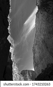 Cliffs soar to the sky as sunlight and shadows dance along the cliffs in this B&W photo
