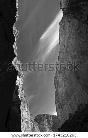 Cliffs soar to the sky as sunlight and shadows dance along the cliffs in this B&W photo
