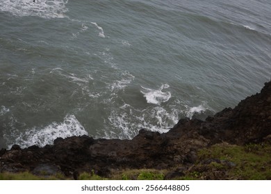 Cliffside View of Ocean Waves Crashing Against Rocky Shore, Overcast Sky, Dramatic Coastal Scenery, Natural Landscape in High Resolution