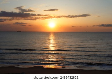 A climactic sunrise over the Virginia Beach shoreline that casts a strong glow over the sky and water.  Off in the background, two cargo ships make their way across the horizon. - Powered by Shutterstock