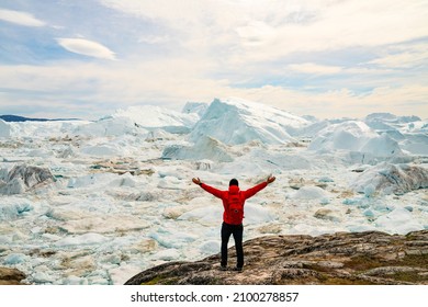 Climate Change and Global Warming Optimism and Positivity Concept. Man on Greenland arms raised in awe of iceberg nature. Melting of glaciers and Greenland ice sheet is a cause of sea levels rise.