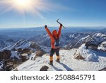 Climber or alpinist at the top of a mountain. A success of mountaineer reaching the summit. Outdoor adventure sports in winter alpine moutain landscape. Sunny day and a climber on a top of a peak.