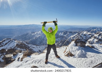 Climber or alpinist at the top of a mountain. A success of mountaineer reaching the summit. Outdoor adventure sports in winter alpine moutain landscape. Sunny day and a climber on a top of a peak. - Powered by Shutterstock