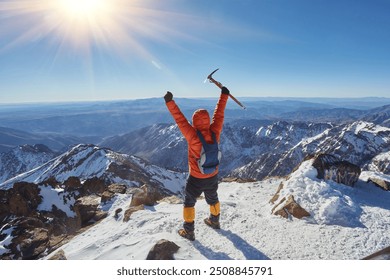 Climber or alpinist at the top of a mountain. A success of mountaineer reaching the summit. Outdoor adventure sports in winter alpine moutain landscape. Sunny day and a climber on a top of a peak. - Powered by Shutterstock