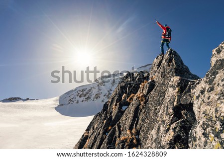 Climber or alpinist at the top of a mountain. A success of mountaineer reaching the summit. Outdoor adventure sports in winter alpine moutain landscape. Sunny day and a climber on a top of a peak.