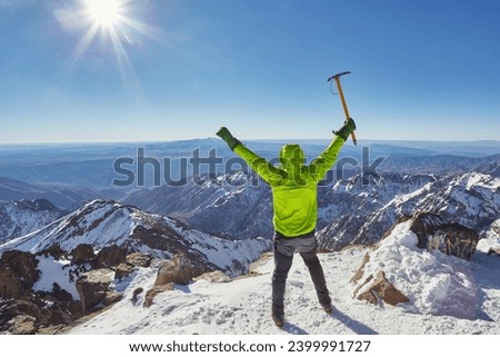 Climber or alpinist at the top of a mountain. A success of mountaineer reaching the summit. Outdoor adventure sports in winter alpine moutain landscape. Sunny day and a climber on a top of a peak.