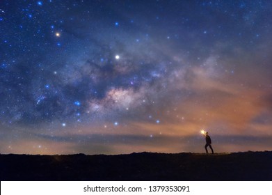 Climber or backpacker with fire in the hand on rocky mountain peak, find the target, search under the stars and Milky Way Galaxy at night, success or winner, leader concept. High iso with Noise. 