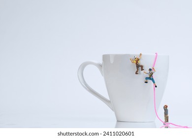 Climber climbing with rope on a white coffee cup, white background, miniature figures scene
​