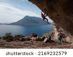 Climber climbs overhanging rock on the background of Telendos island on sunny day. Kalymnos island, Greece.