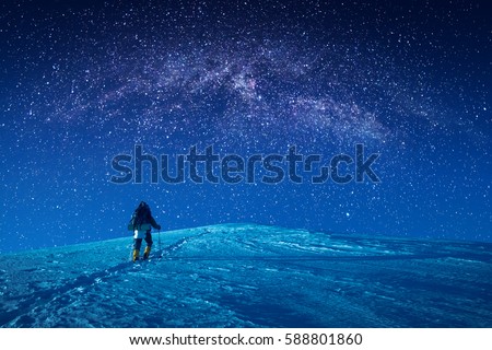 A climber climbs up a snowy slope at night. Milky way in a starry sky above the mountain top.