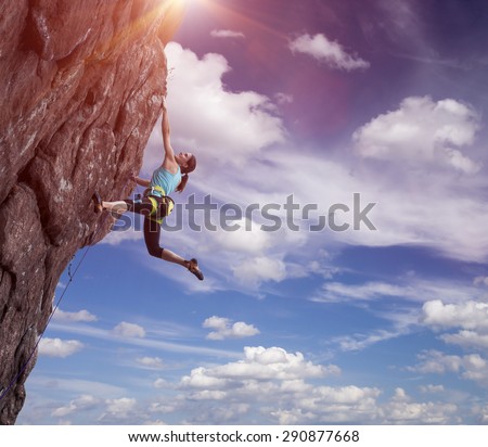 Climber hanging on her hand.
Elegant female athlete hanging at top of dangerous peak equipped with gear rope harness blue sky and terrific clouds on background and sunbeams shining from above