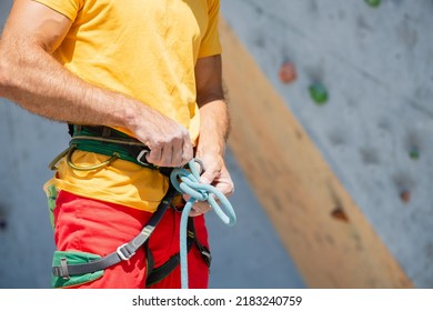 A climber knits a knot. A man prepares to climb a climbing route. Insurance and safety in rock climbing. Safety rope. Node eight. - Powered by Shutterstock