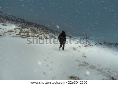 Climber reaching the summit of the mountain during a hard snow storm.