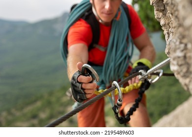 Climber snaps the safety carabiner on the rope. A climber on a cliff ties a safety knot - Shutterstock ID 2195489603