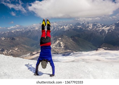 Climber standing upside down on his hands on top of the mountain