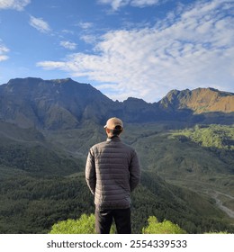 climber stands looking at forest trees, expanse of mountains and clear sky - Powered by Shutterstock