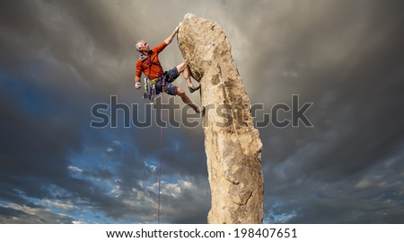 Climber struggles for his next grip on the edge of a challenging cliff.