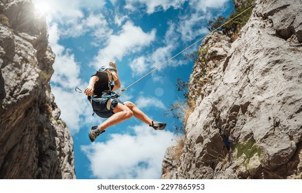 Climber teenage boy in protective helmet jumping on vertical cliff rock wall using rope Belay device, climbing harness in Paklenica canyon in Croatia. Active extreme sports time spending concept - Powered by Shutterstock