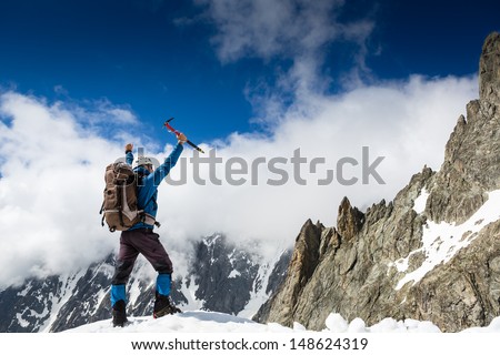 Climber at the top of a rock with his hands raised enjoy sunny day 