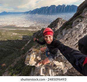 Climber wearing a red helmet takes a selfie while scaling a rocky cliff with Monterrey's expansive cityscape and mountain range in the background. The clear sky and sunlight enhance the dramatic lands - Powered by Shutterstock