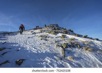 Climbers Ascending A Snowe Ridge To The Summit Of A High Peak. Blue Sky, Beautiful Clouds And Winter Mountians Around. Winter Hiking Adventure.