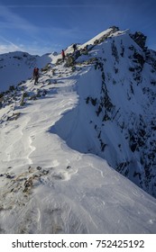 Climbers Ascending A Snowe Ridge To The Summit Of A High Peak. Blue Sky, Beautiful Clouds And Winter Mountians Around. Winter Hiking Adventure.