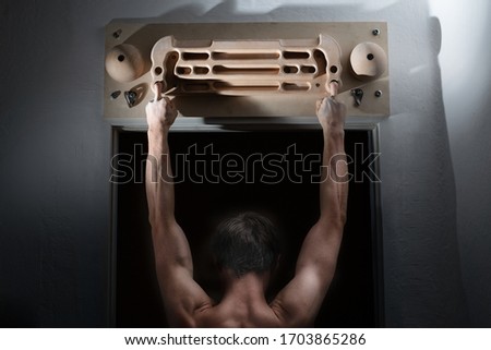 Climber's strong back and fingers in magnesia on the fingerboard. Training in rock climbing. Back view. Man is doing a training on climbing fingerboard. Stay at home. 