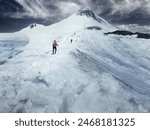 Climbers with trekking poles and crampons walk up icy slope to top of snow capped mountain at sunny day, Caucasus Mountains