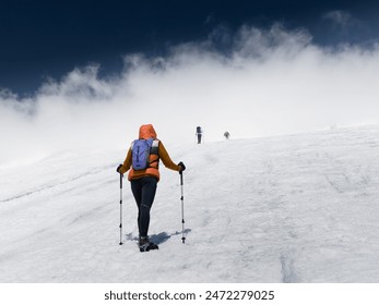 Climbers with trekking poles and crampons walk up snow slope into bright white cloud on top of mountain at sunny day, Caucasus - Powered by Shutterstock