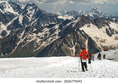 Climbers Are Walking Along A Mountain Range. A Group Of Tourists With Backpacks Go Down A Snow-covered Ice Slope.