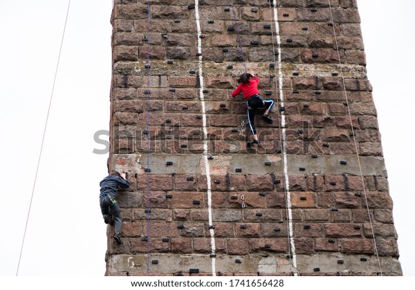 Climbers who climb a steep wall. Two\
people climb the support of the old railway\
bridge.