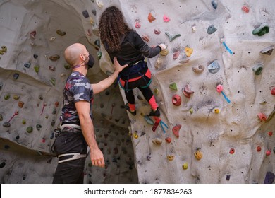 Climbing instructor wearing protective face mask assisting a young woman student during the climbing in a climbing wall. Learning process in the new normal. - Powered by Shutterstock