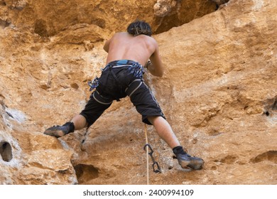 Climbing the rugged rockface. Rearview of rugged bare chested rock climber climbing a rockface.