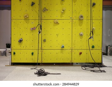  Climbing Simulator ,Fit Man Looking Up At Rock Climbing Wall At The Gym, Yellow Concrete Wall Background And A Carabiner Hook.