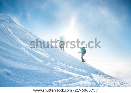 climbing a snow-covered mountain during a snow storm, two women in winter trekking, climbers climb to the top of the mountain in winter