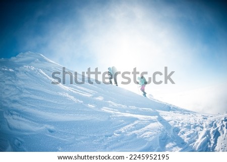 climbing a snow-covered mountain during a snow storm, two women in winter trekking, climbers climb to the top of the mountain in winter