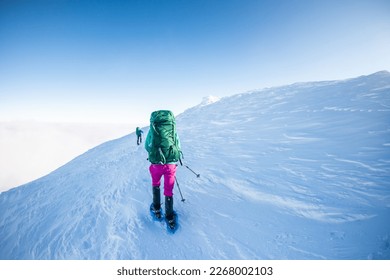 climbing a snow-covered mountain, two women in winter trekking, climbers climb to the top of the mountain in winter - Shutterstock ID 2268002103