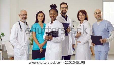 Clinic or hospital staff at work. Diverse team of happy smiling doctors, clinicians, therapists, cardiologists in scrubs and white coat uniform standing together, holding clipboards, looking at camera
