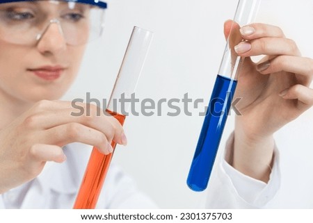 Clinic laboratory analysis and testing. Young woman in protective goggles holding test tube with color liquid. Laboratory assistant comparing samples in test tubes. Biochemistry or chemical research.