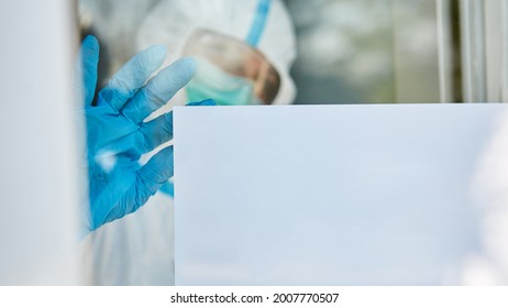 Clinic Staff In Protective Clothing Fastened Notice Board To Clinic Door Because Of Coronavirus And Covid-19