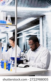Clinical microbiologist operating compound microscope does detailed sample observation in controlled laboratory environment. Biotechnology research facility expert studies tissue under optical device