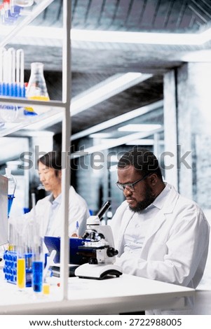 Clinical microbiologist operating compound microscope does detailed sample observation in controlled laboratory environment. Biotechnology research facility expert studies tissue under optical device