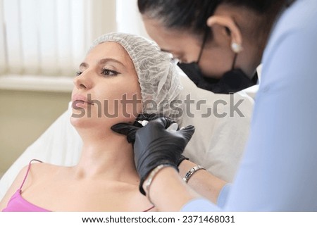 clinical setting, cosmetic professional carefully administers filler injection into patient's jowls, part procedure aimed at contouring face and reducing masseter lines.
