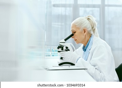 Clinical Test. Female Scientist Working In Laboratory. Mature Woman Doctor Researching, Looking In Microscope, Working In Light Medical Laboratory. Healthcare And Medicine. High Resolution