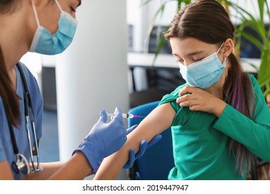 Clinical trial for new modern Covid vaccine during global pandemic. Little girl in medical face mask getting injection at hospital. Doctor or nurse giving shot to female patient with syringe
