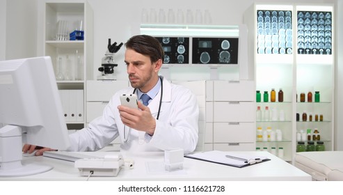 Clinician Doctor Man Working With Computer And Mobile Phone Searching Electronic In Hospital Cabinet Or Healthcare Center Room