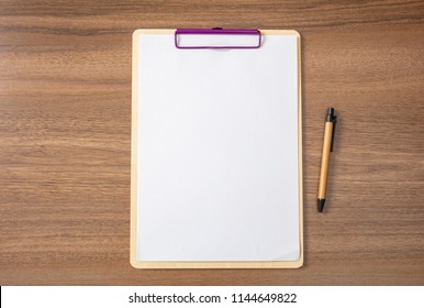 Clipboard With Blank Paper Sheet And A Pen On Wooden Desk, Space For Text, Top View