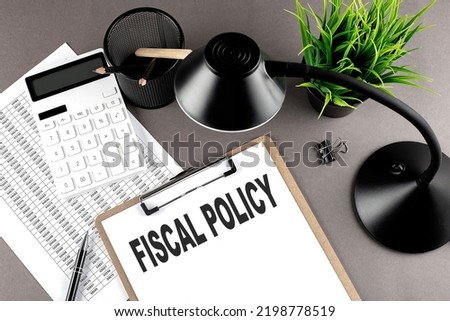 Clipboard ,chart and calculator, lamp and workspace accessories on grey table. Top view , text FISCAL POLICY