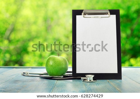 Clipboard with green apple and stethoscope on a blue wooden table against the background blur green leaves bokeh