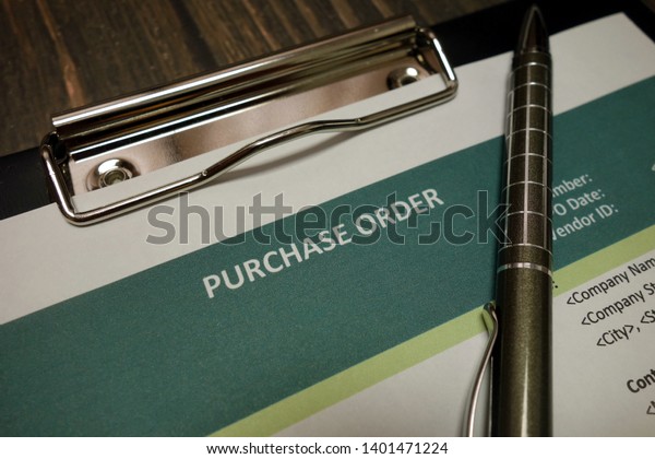 Clipboard with purchase order and pen on\
wooden desk\
background